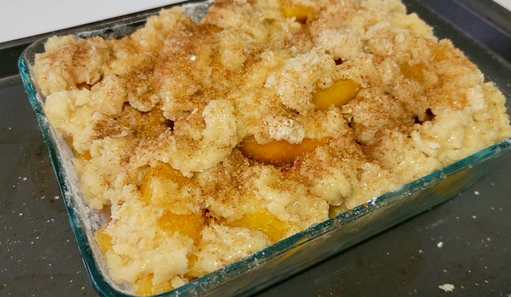 This Easy Homemade Peach Cobbler is perfect year-round because it uses Frozen Peaches! It features a buttery cakey topping with cinnamon.